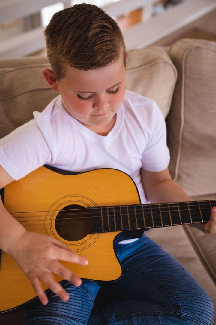Caucasian boy playing guitar sitting on the couch at home - Free Images, Stock Photos and Pictures on Pikwizard.com