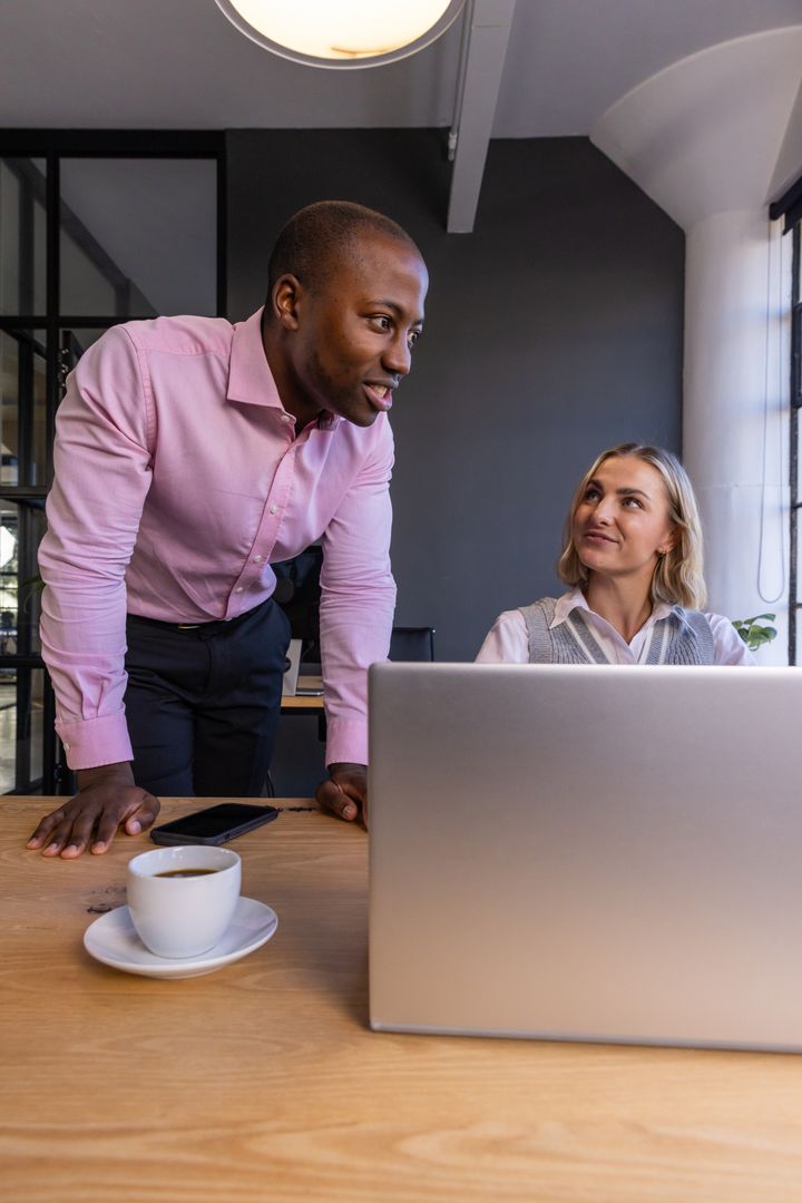 Diverse Coworkers Discussing Project Over Laptop in Modern Office