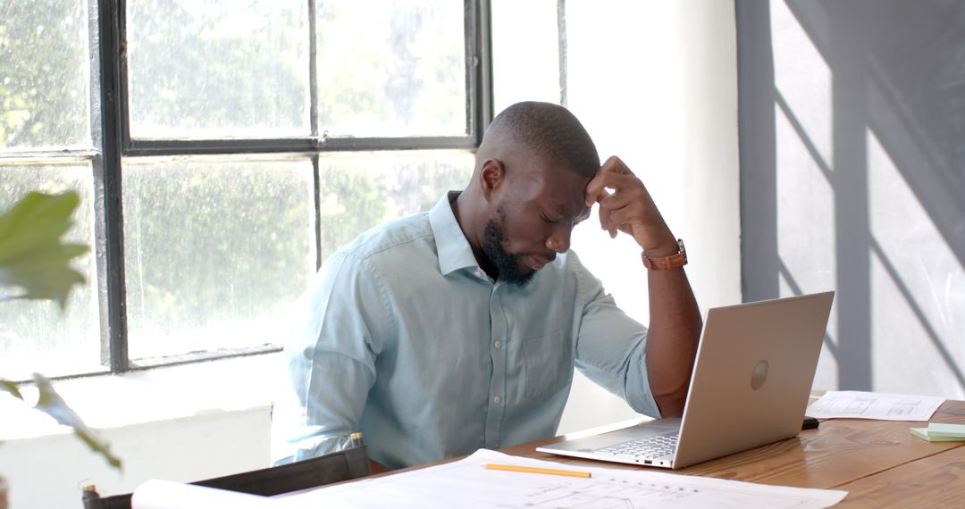 Architect Examining Project Plans on Laptop in Sunlit Office