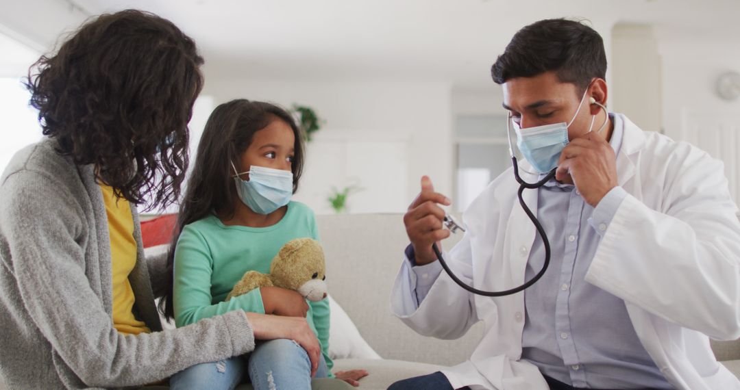 Hispanic male doctor holding stethoscope talking to mother and daughter at home wearing face masks - Free Images, Stock Photos and Pictures on Pikwizard.com