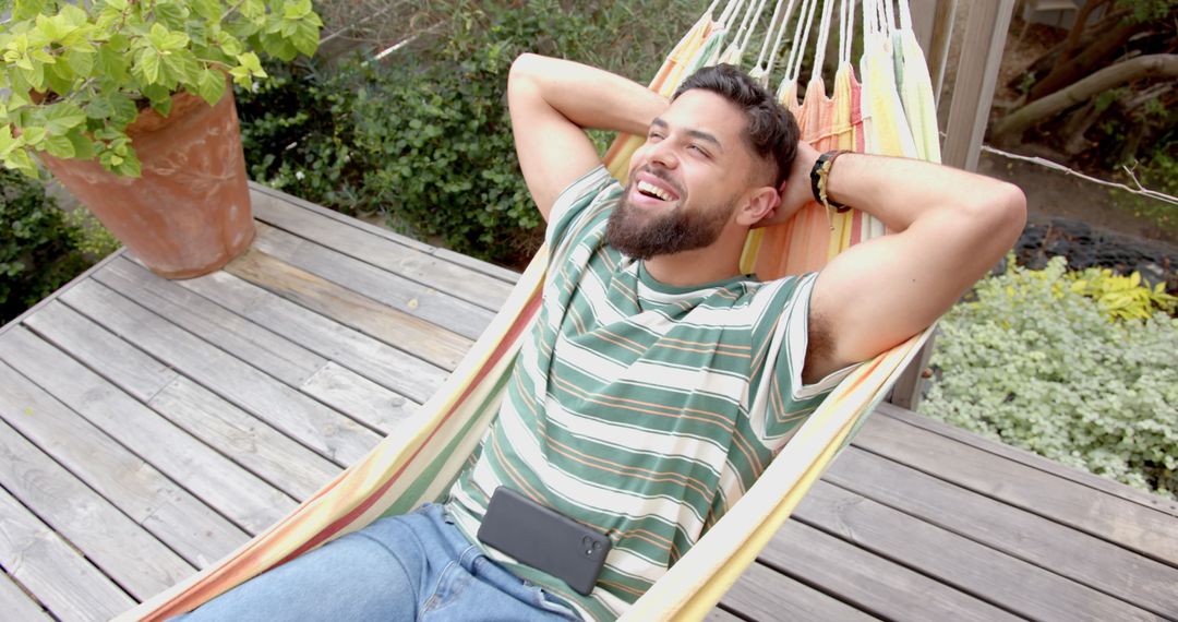 Smiling Man Relaxing in Hammock with Smartphone Outdoors
