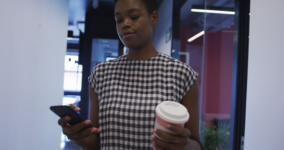 African American Woman Walking in Office Using Smartphone and Holding Coffee - Free Images, Stock Photos and Pictures on Pikwizard.com