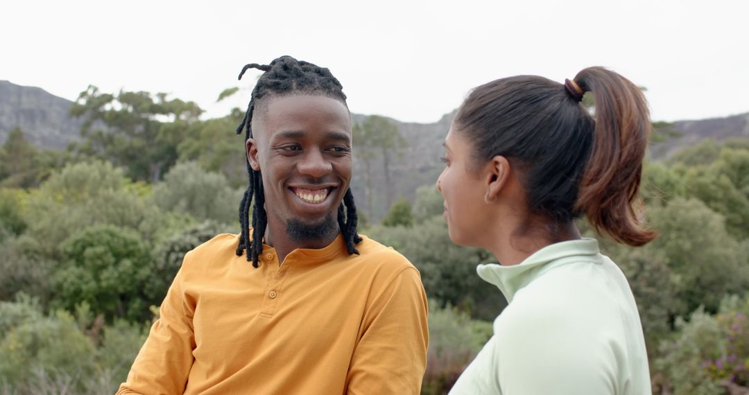 Diverse couple smiling and talking during nature outing, dreadlocked man in mustard henley