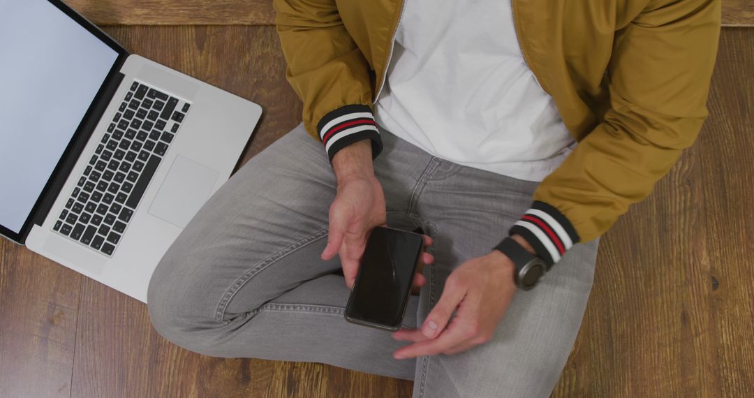 Man Using Smartphone Sitting Next to Laptop on Wooden Floor - Free Images, Stock Photos and Pictures on Pikwizard.com