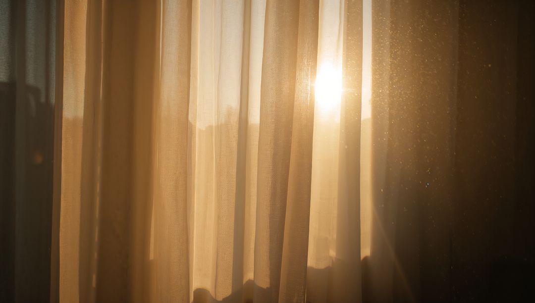 Sunlight pouring through sheer beige curtains casting warm glow and floating dust