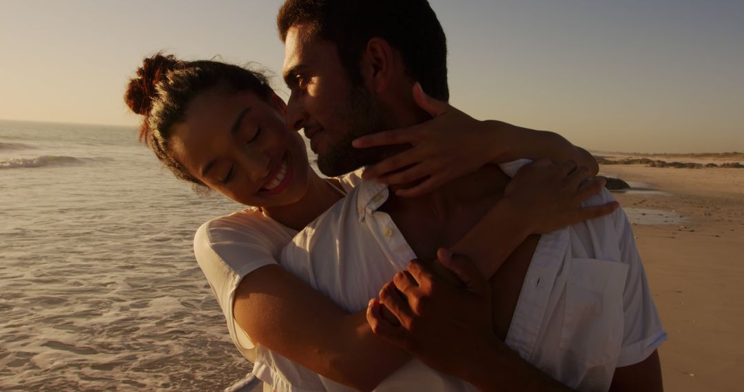 Biracial couple embraces lovingly on a beach at sunset - Free Images, Stock Photos and Pictures on Pikwizard.com