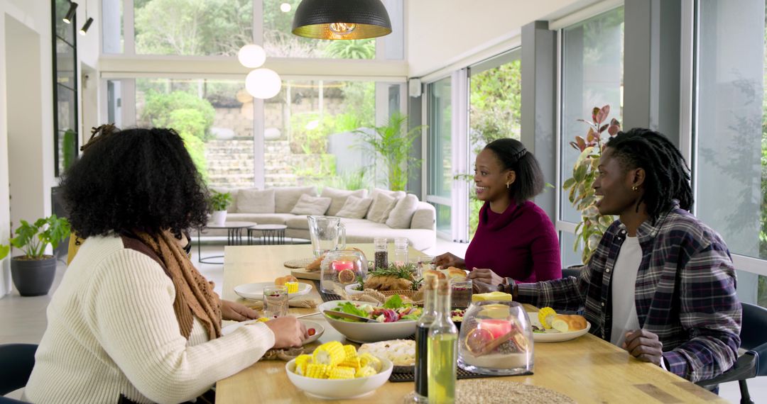 Black Friends Sharing Casual Lunch at Wooden Dining Table in Sunlit Modern Open-Plan Home