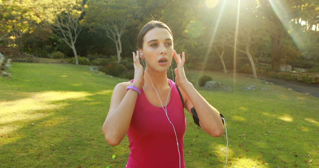 Young Woman Adjusting Earphones While Jogging in Park - Free Images, Stock Photos and Pictures on Pikwizard.com