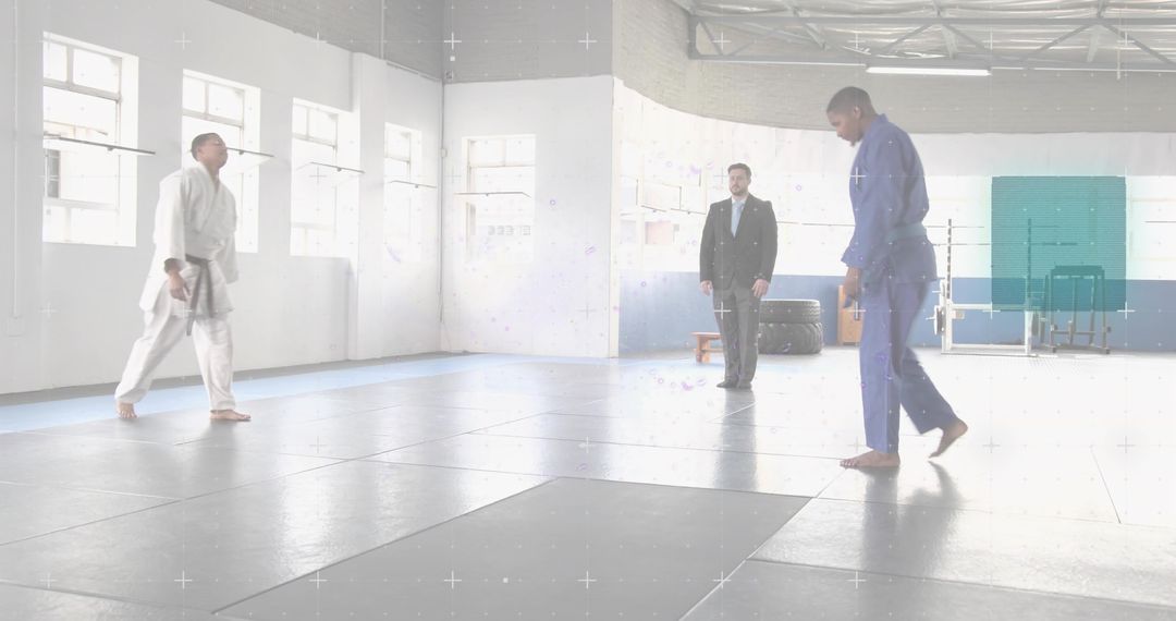 Athlete stepping in blue gi across bright dojo mats with coach observing