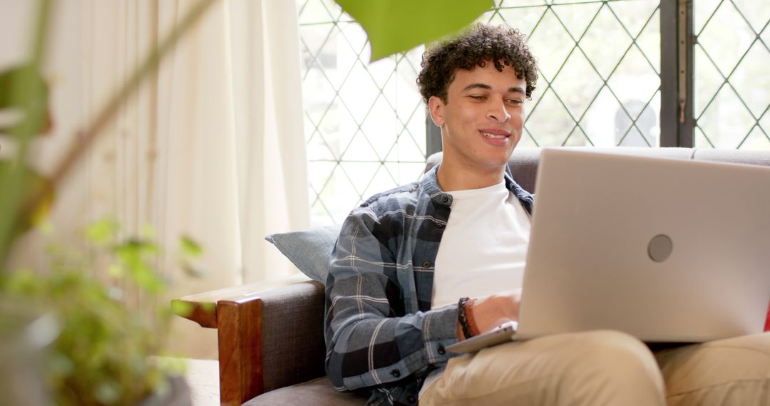 Young Man Smiling Using Laptop on Sofa in Bright Living Room - Free Images, Stock Photos and Pictures on Pikwizard.com