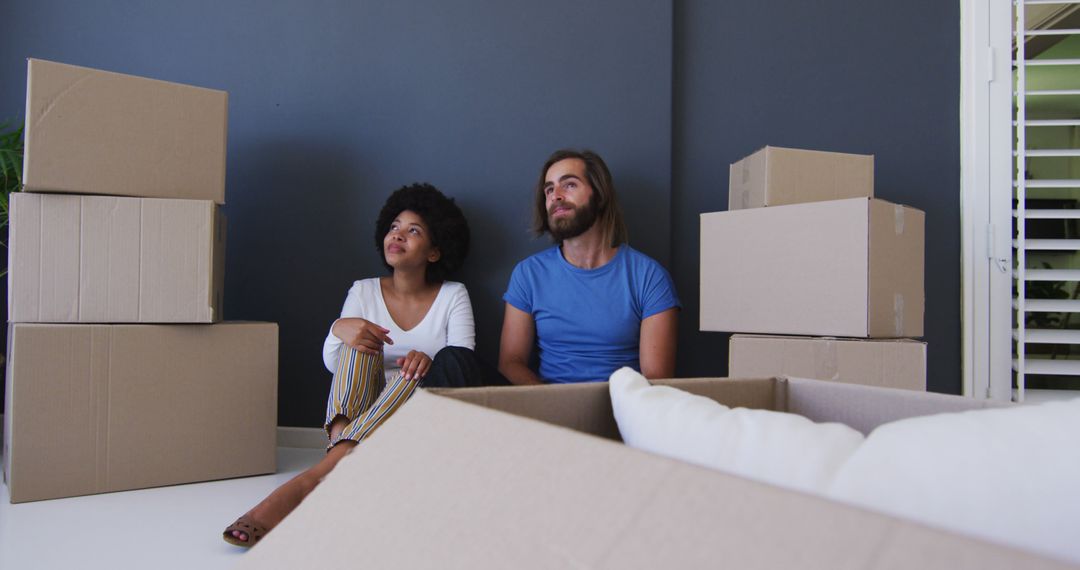 Biracial couple sitting in between cardboard boxes at new apartment house - Free Images, Stock Photos and Pictures on Pikwizard.com