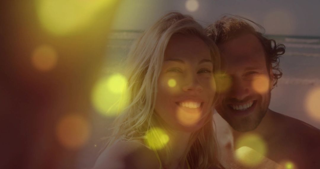 Smiling couple taking beach selfie at sunset with golden bokeh and backlit glow