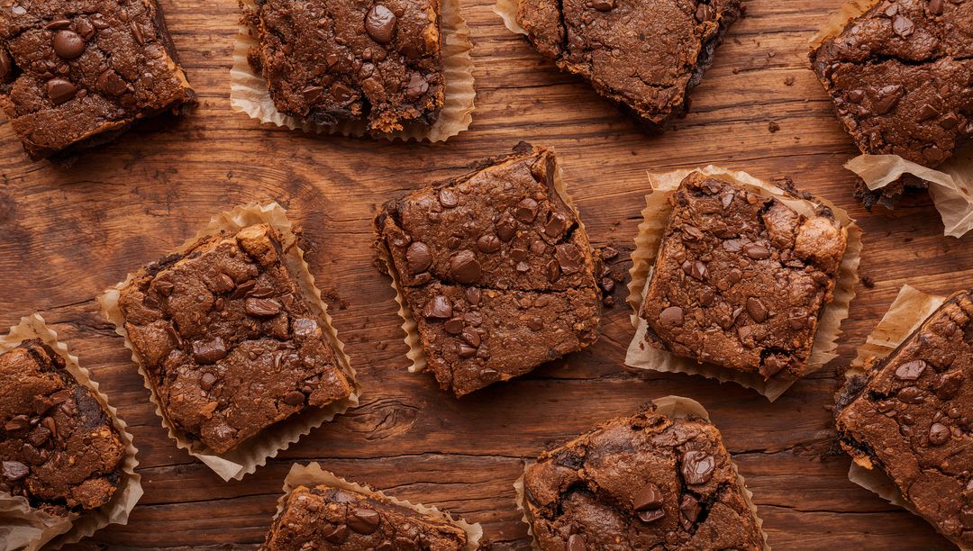 Fudgy Chocolate Brownie Squares on Rustic Wood with Parchment Liners and Chocolate Chips