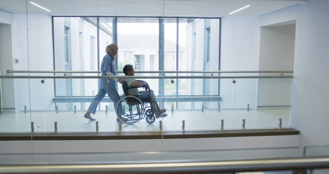 Caregiver Pushing Man in Wheelchair Through Modern Hospital Hallway - Free Images, Stock Photos and Pictures on Pikwizard.com