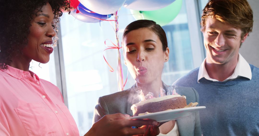 Businesswoman Blowing Out Birthday Candles with Colleagues in Office - Free Images, Stock Photos and Pictures on Pikwizard.com