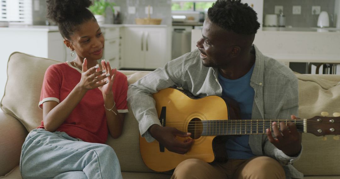 Image of happy african american couple sitting on sofa, singing and playing guitar - Free Images, Stock Photos and Pictures on Pikwizard.com