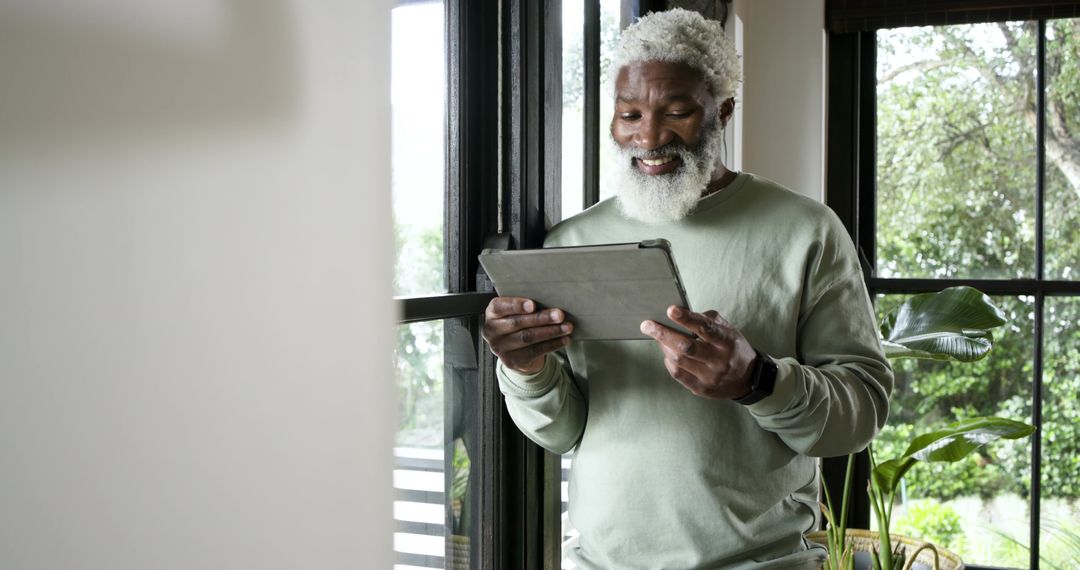 Senior Man Enjoying Technology on Tablet by Window at Home