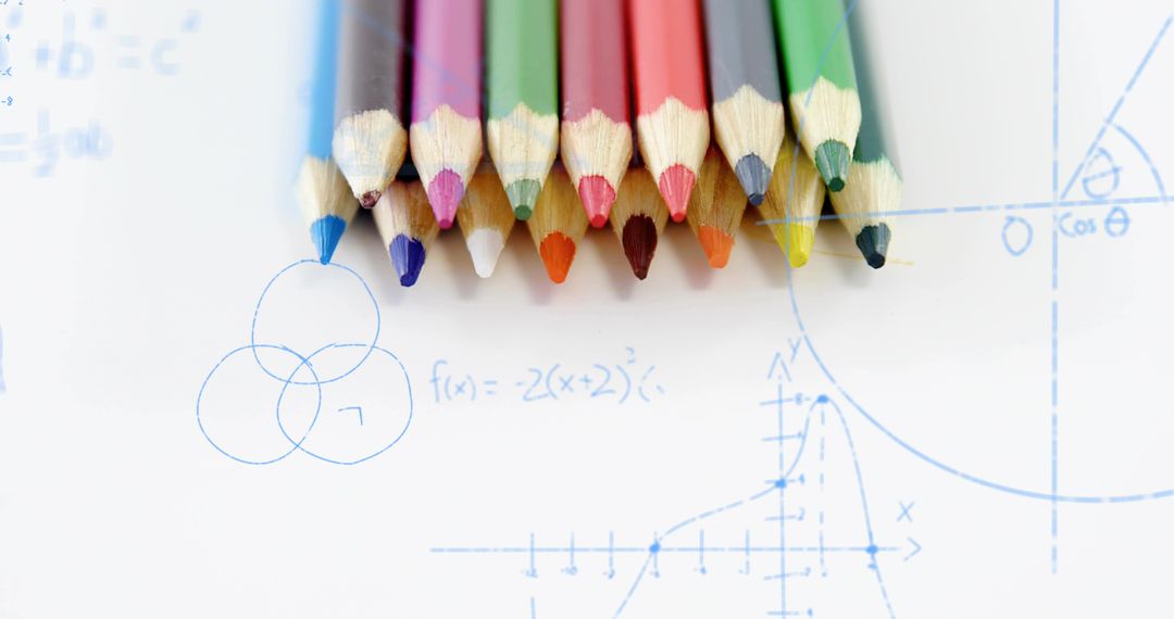 Colored pencils lining up on study paper with blue math sketches for creative learning