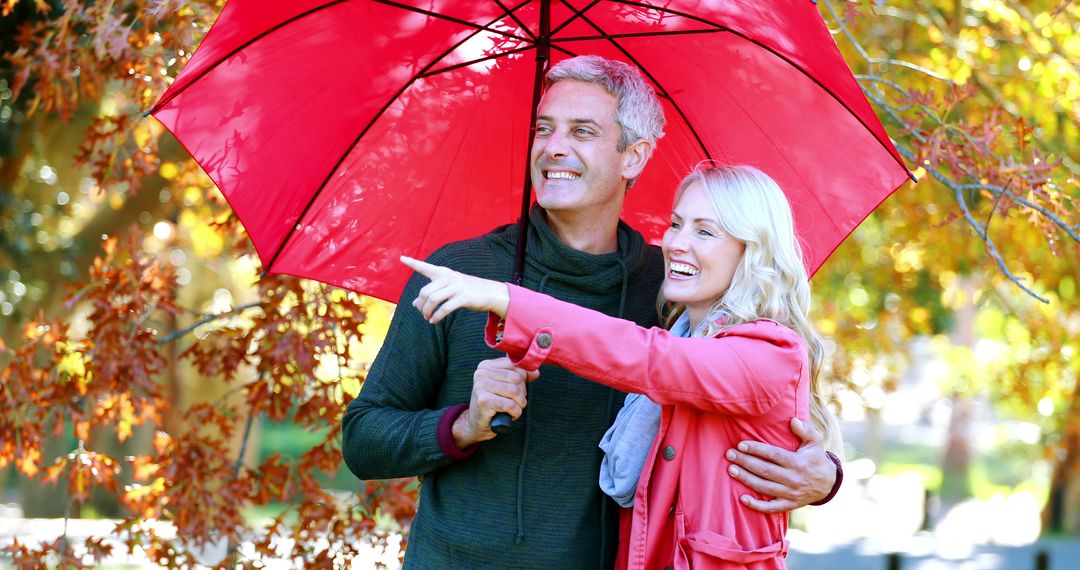 Happy Couple Enjoying Autumn Weather Under Red Umbrella - Free Images, Stock Photos and Pictures on Pikwizard.com