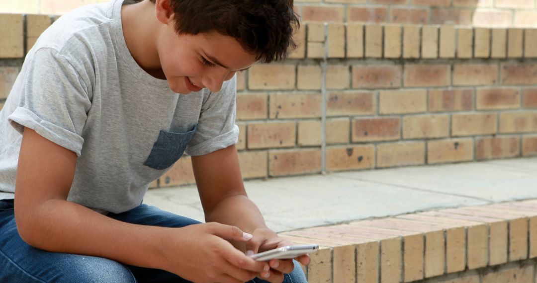 Teenager Engaged with Smartphone Outdoors on Sunny Day - Free Images, Stock Photos and Pictures on Pikwizard.com