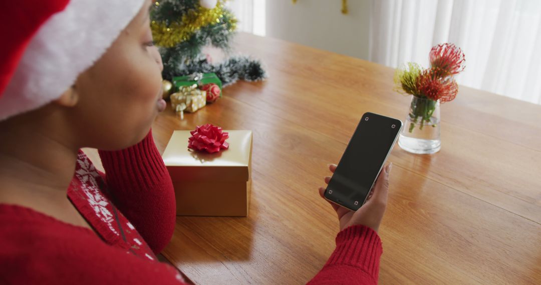 Woman Wearing Santa Hat Using Smartphone with Christmas Gifts on Wooden Table - Free Images, Stock Photos and Pictures on Pikwizard.com