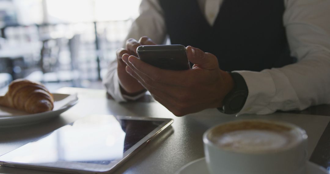 Businessman using smartphone in coffee shop with tablet and croissant - Free Images, Stock Photos and Pictures on Pikwizard.com