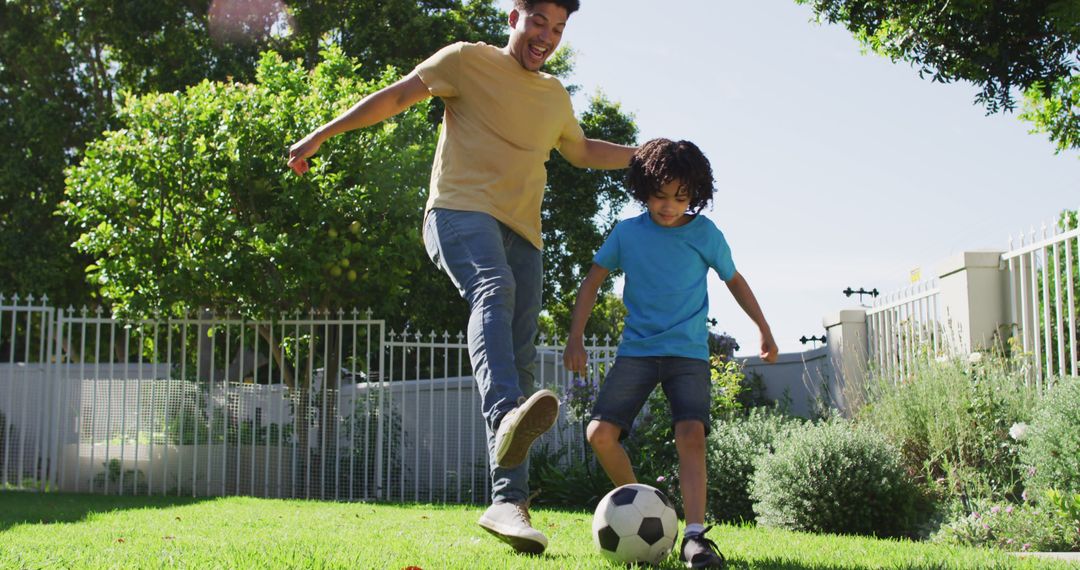 Happy biracial man and his son playing football in garden - Free Images, Stock Photos and Pictures on Pikwizard.com