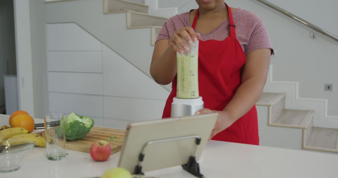 Woman in Red Apron Blending Healthy Green Smoothie in Modern Kitchen - Free Images, Stock Photos and Pictures on Pikwizard.com