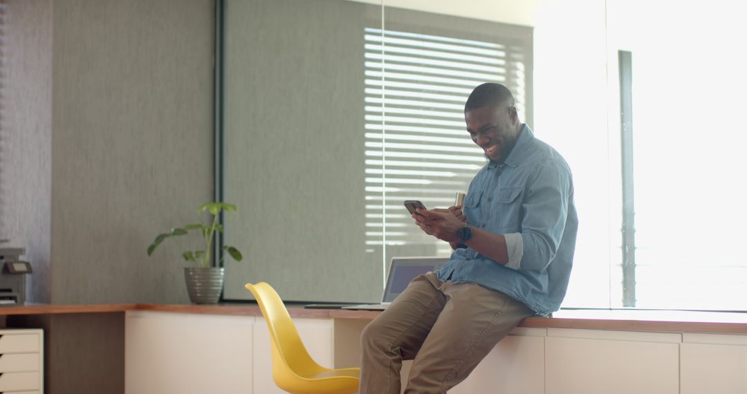 Young Professional Relaxing in Office Using Smartphone Near Laptop