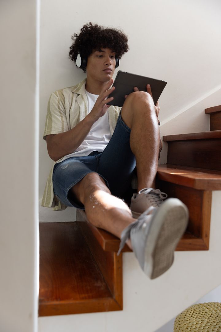 Young Man Relaxing on Stairs with Tablet and Headphones at Home