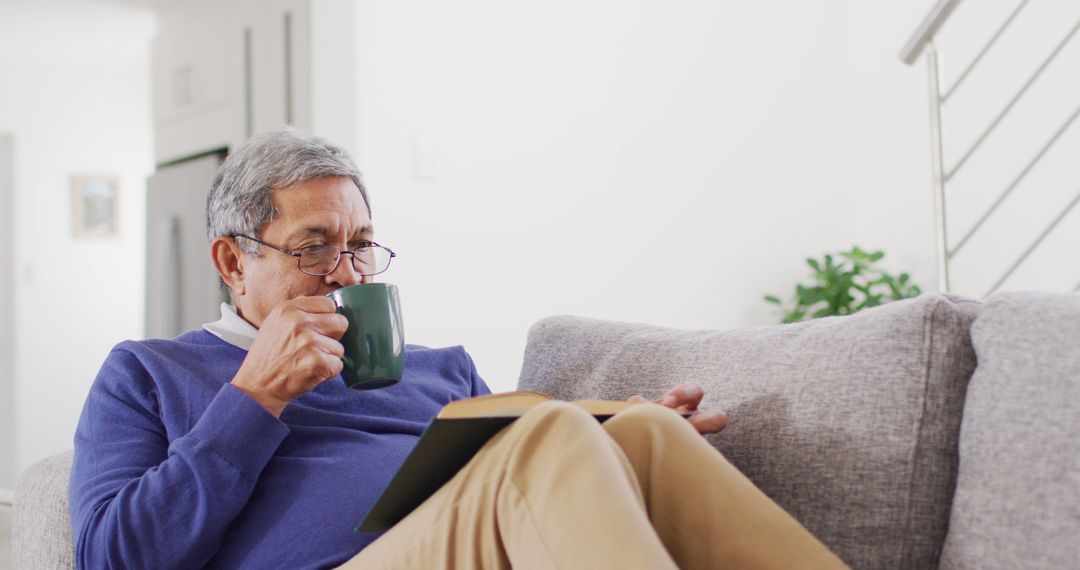 Image of happy senior biracial man drinking coffee and reading book on couch at home - Free Images, Stock Photos and Pictures on Pikwizard.com