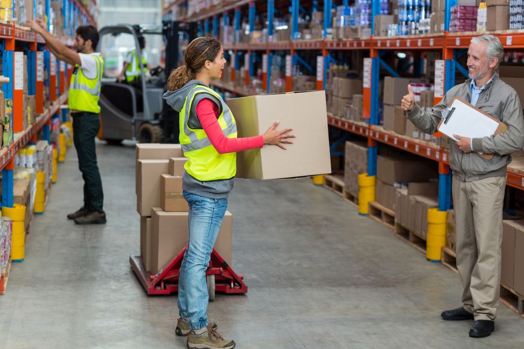 Warehouse manager showing thumbs up to female worker while carrying cardboard boxes - Free Images, Stock Photos and Pictures on Pikwizard.com