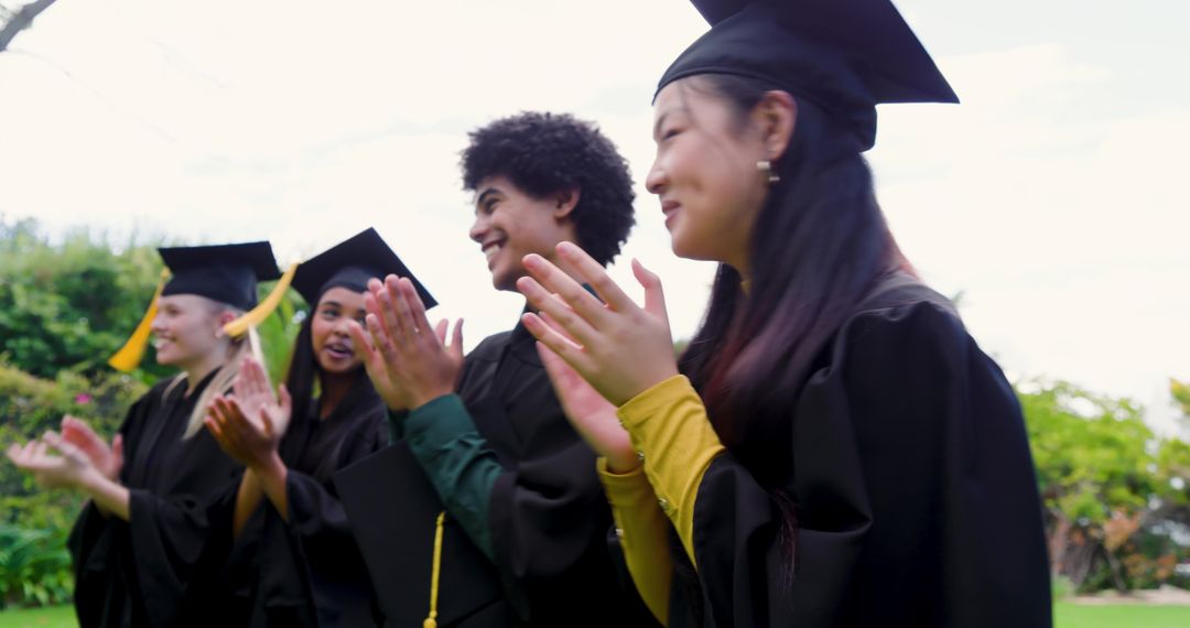 Multicultural graduates applauding during outdoor commencement on campus