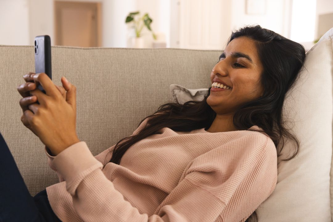 South Asian Woman Relaxing on Sofa Using Smartphone at Home