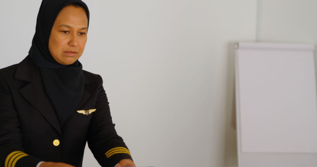 A middle-aged Asian woman in a pilot uniform is focused on her task, with copy space - Free Images, Stock Photos and Pictures on Pikwizard.com