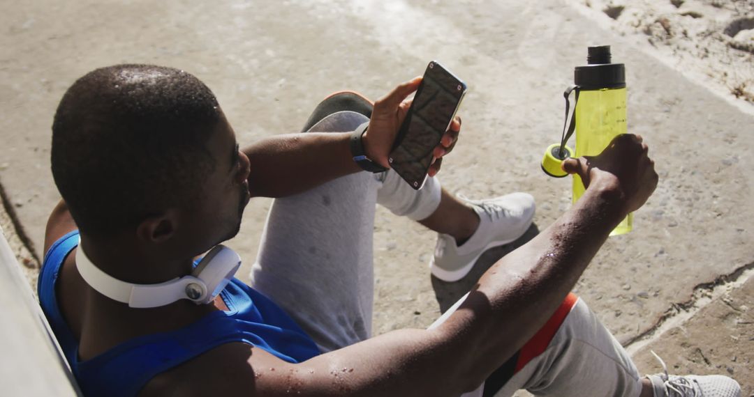 Man Using Smartphone and Hydrating During Outdoor Workout Break