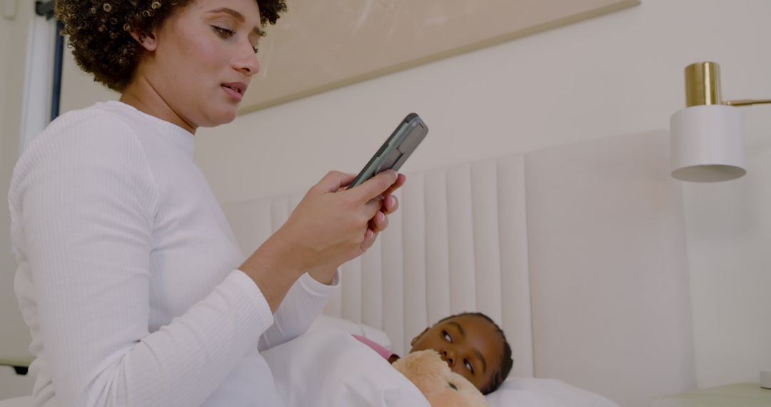 Mother Checking Smartphone Beside Child Cuddling Teddy Bear
