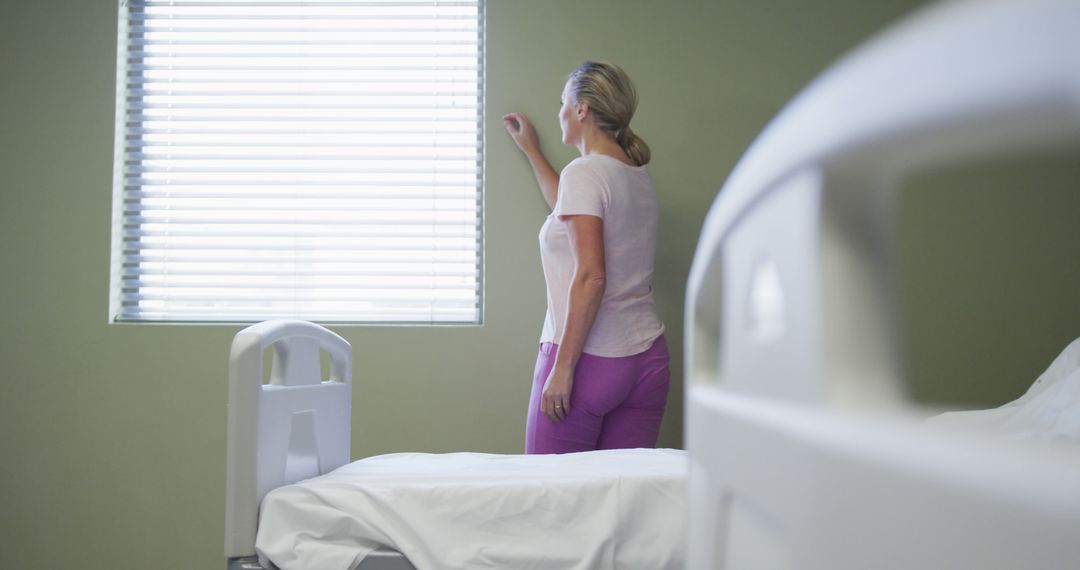 Caucasian female patient standing in hospital room looking at window - Free Images, Stock Photos and Pictures on Pikwizard.com