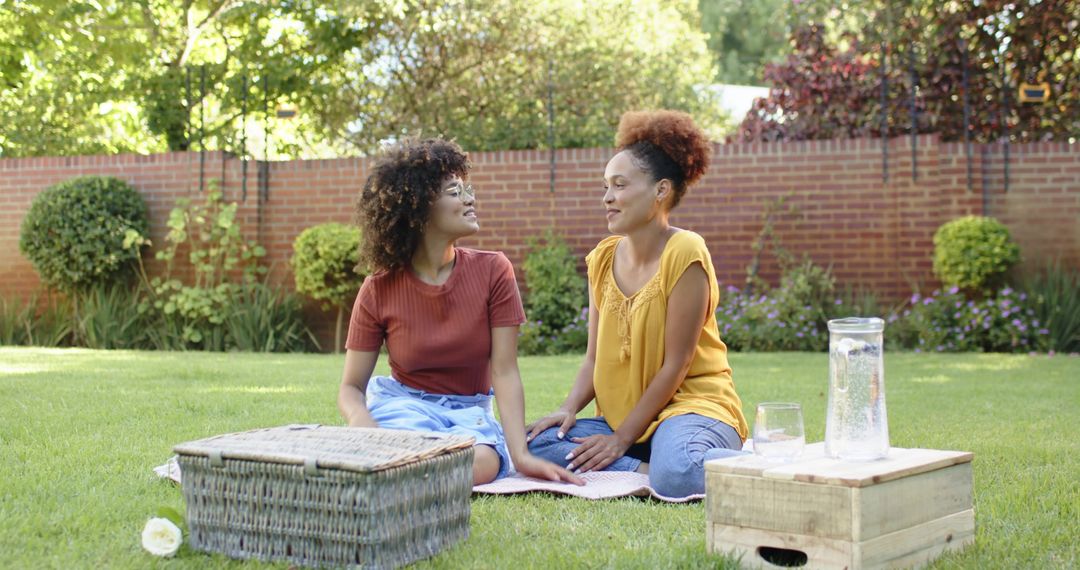 Diverse Women Chatting on Picnic Blanket in Sunny Backyard Relaxing with Basket, Pitcher