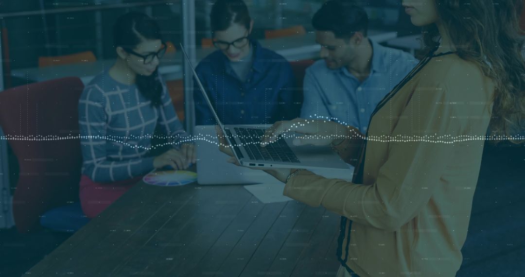 Standing woman presenting with laptop to team in office, data overlay, collaboration