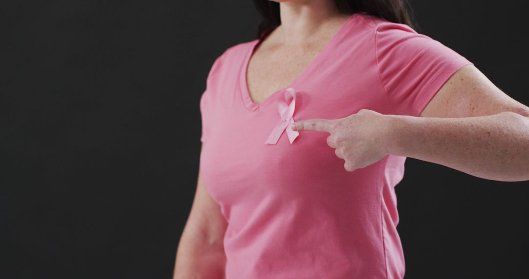 Woman Wearing Pink T-Shirt Pointing at Breast Cancer Awareness Ribbon - Free Images, Stock Photos and Pictures on Pikwizard.com