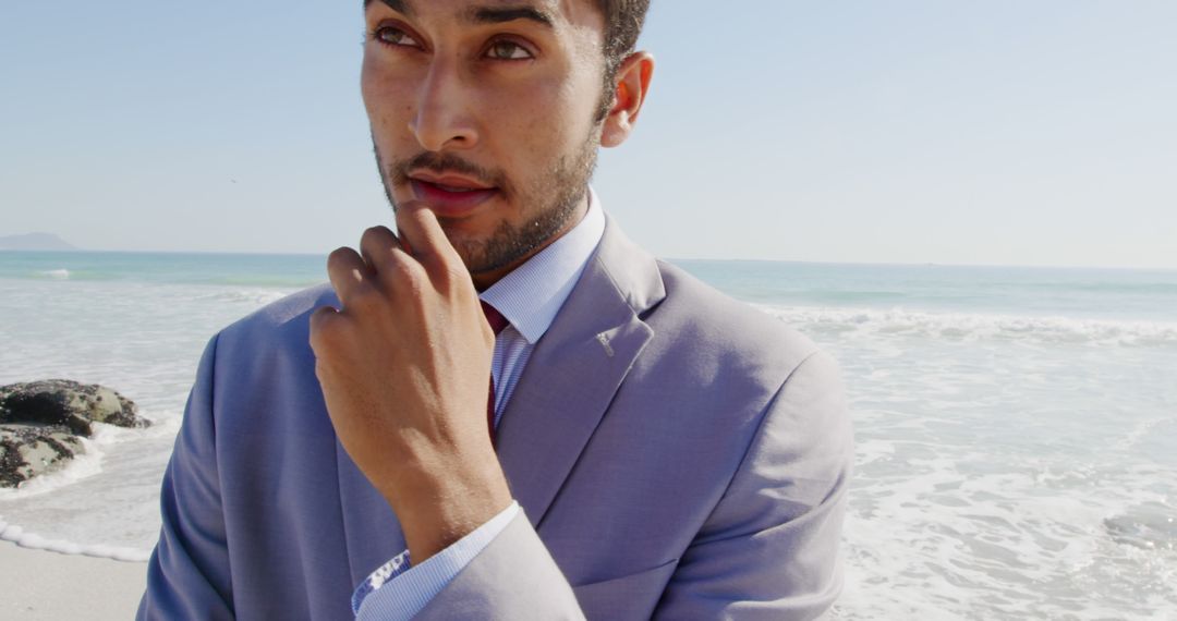 A young biracial man wearing suit stands on beach, touching his lips - Free Images, Stock Photos and Pictures on Pikwizard.com
