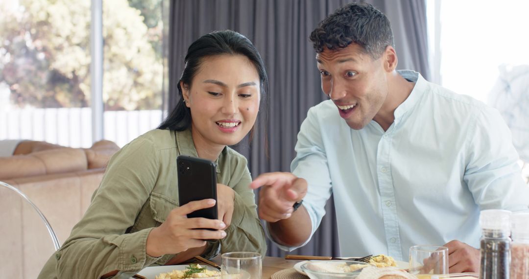 Couple sharing surprise while checking phone over casual breakfast at cozy home table