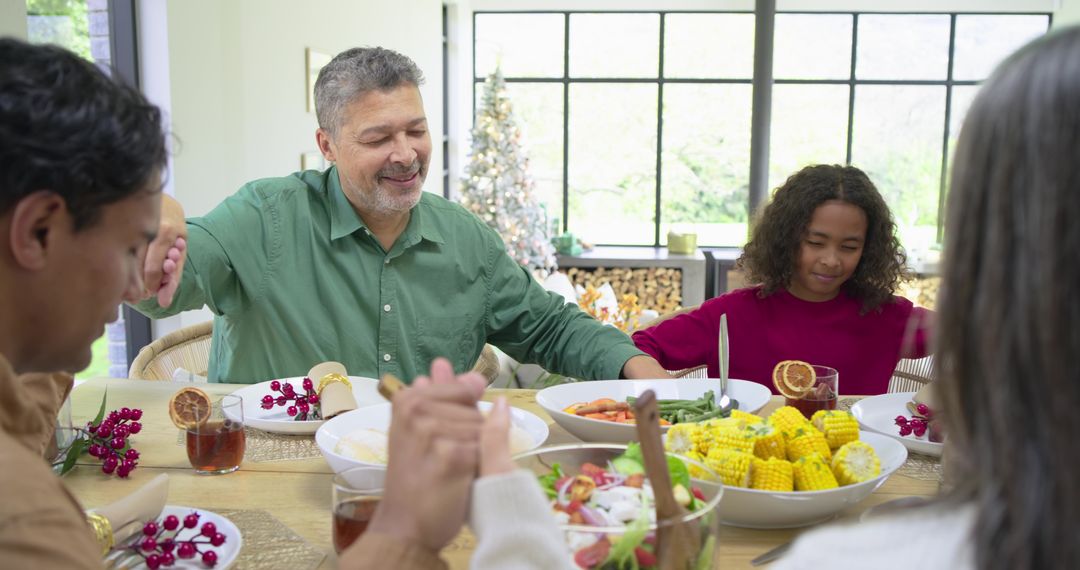Multigenerational diverse family holding hands around festive dinner with corn and salad