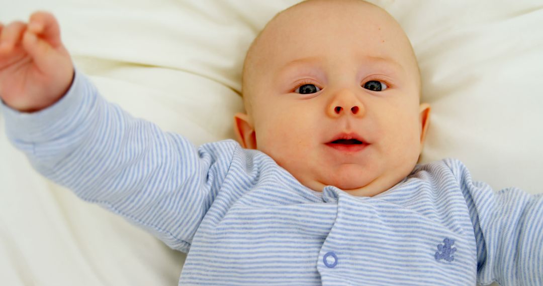 Cute Baby in Blue Striped Pajamas with Arms Outstretched on White Bedding - Free Images, Stock Photos and Pictures on Pikwizard.com