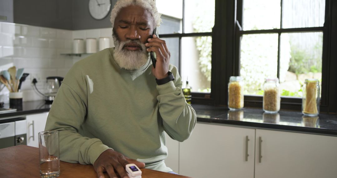 Senior Man Monitoring Pulse with Oximeter While on Phone in Kitchen