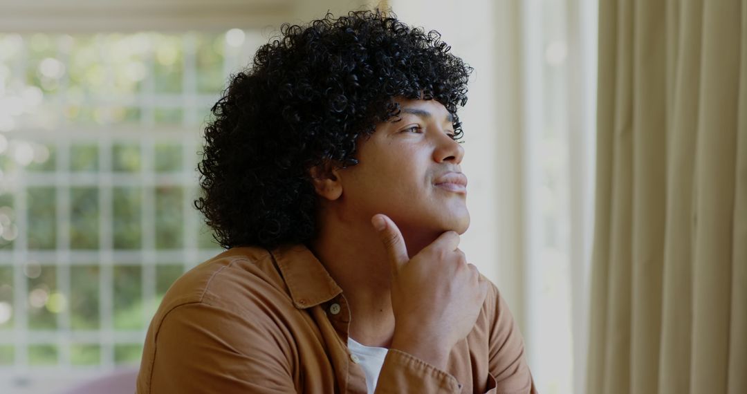 Smiling Man with Curly Hair Contemplating by a Window Indoors