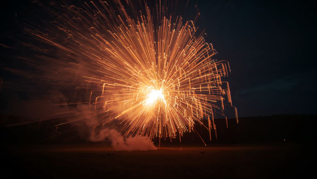 Golden Firework Explosion Illuminating Night Sky Over Field