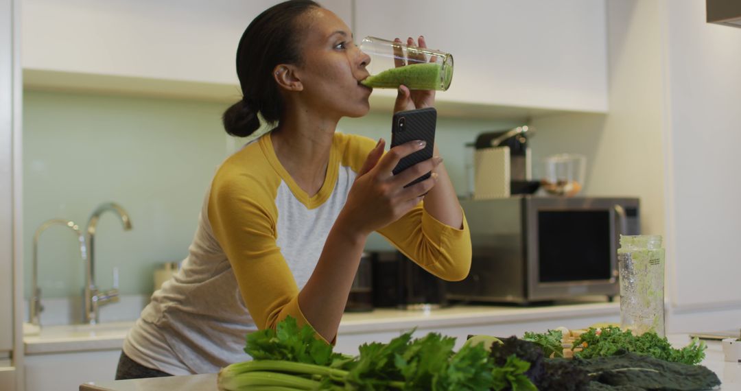 Woman Drinking Green Smoothie While Using Smartphone in Modern Kitchen - Free Images, Stock Photos and Pictures on Pikwizard.com