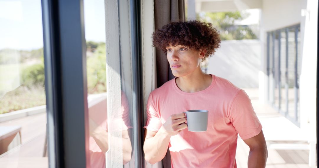 Curly-haired Man Holding Mug Reflecting by Window at Home